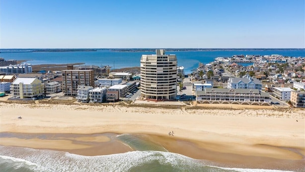 Un paisaje urbano costero con un hotel de diseño curvo destacado, propiedades frente al mar y una vista despejada del océano.