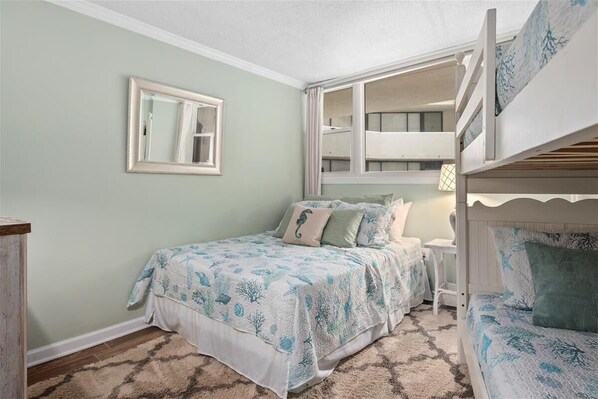 Un dormitorio con una cama litera, una cama individual con ropa de cama a juego, una mesita de noche, un espejo y una ventana con cortinas.