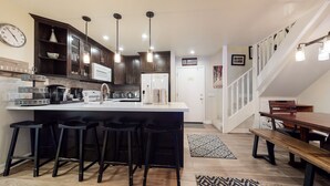 A modern kitchen with dark wooden cabinets, a white island with bar stools, a stainless steel refrigerator, and a staircase leading to a loft bedroom. - Bright Unit, Quiet Location, Near Mountain Bike Trails, Balcony. On-site Pool (Mammoth Lakes)