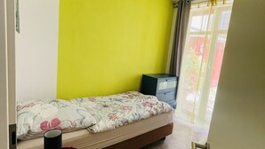 Ein kleiner, farbenfroher Raum mit einem Einzelbett, einem Tisch und einem Fenster mit Vorhängen.