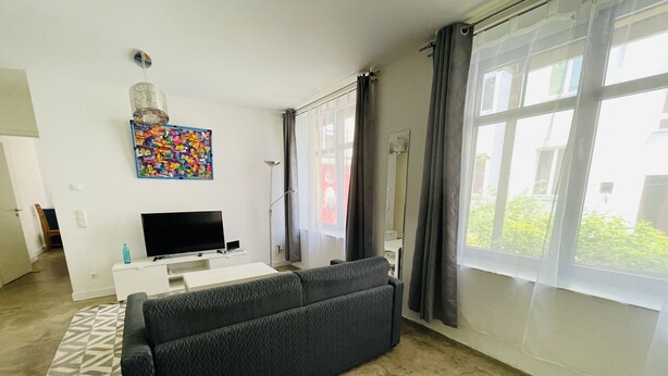 Ein modernes Wohnzimmer mit einer schwarzen Couch, einem Flachbildfernseher, einem weißen Couchtisch und einem farbenfrohen abstrakten Gemälde an der Wand.