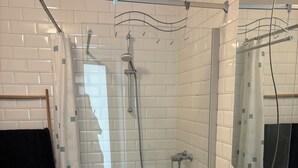 Ein Badezimmer mit weißen Fliesen, einer Dusche mit Glastür, einem Waschbecken mit Spiegel und einem Handtuchhalter.