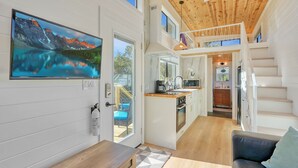 A modern interior with a kitchen, dining area, and a staircase leading to an upper level. - Starlight Casita | Modern Tiny House (Fischer)