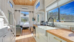 A modern kitchen with a large window, wooden ceiling, and a dining area with a sofa. - Starlight Casita | Modern Tiny House (Fischer)