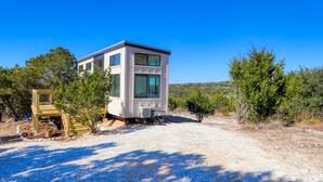 A modern, single-story building with large windows, a wooden deck, and a gravel driveway. - Starlight Casita | Modern Tiny House (Fischer)