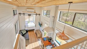 A compact, modern interior with a wooden ceiling, a kitchenette, a dining area, and a large window offering a view of the outdoors. - Starlight Casita | Modern Tiny House (Fischer)