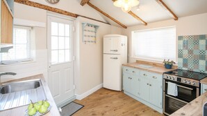 A kitchen with wooden beams, a white refrigerator, a stove, and a clock on the wall. - Bryn Coed (Porthmadog)