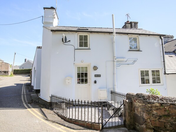 A white two-story house with a white door, a satellite dish, and a small garden.