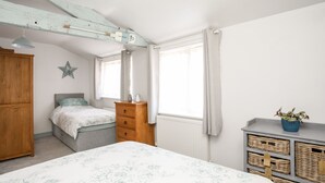 A bedroom with a bed, dresser, and a window with curtains. - Bryn Coed (Porthmadog)