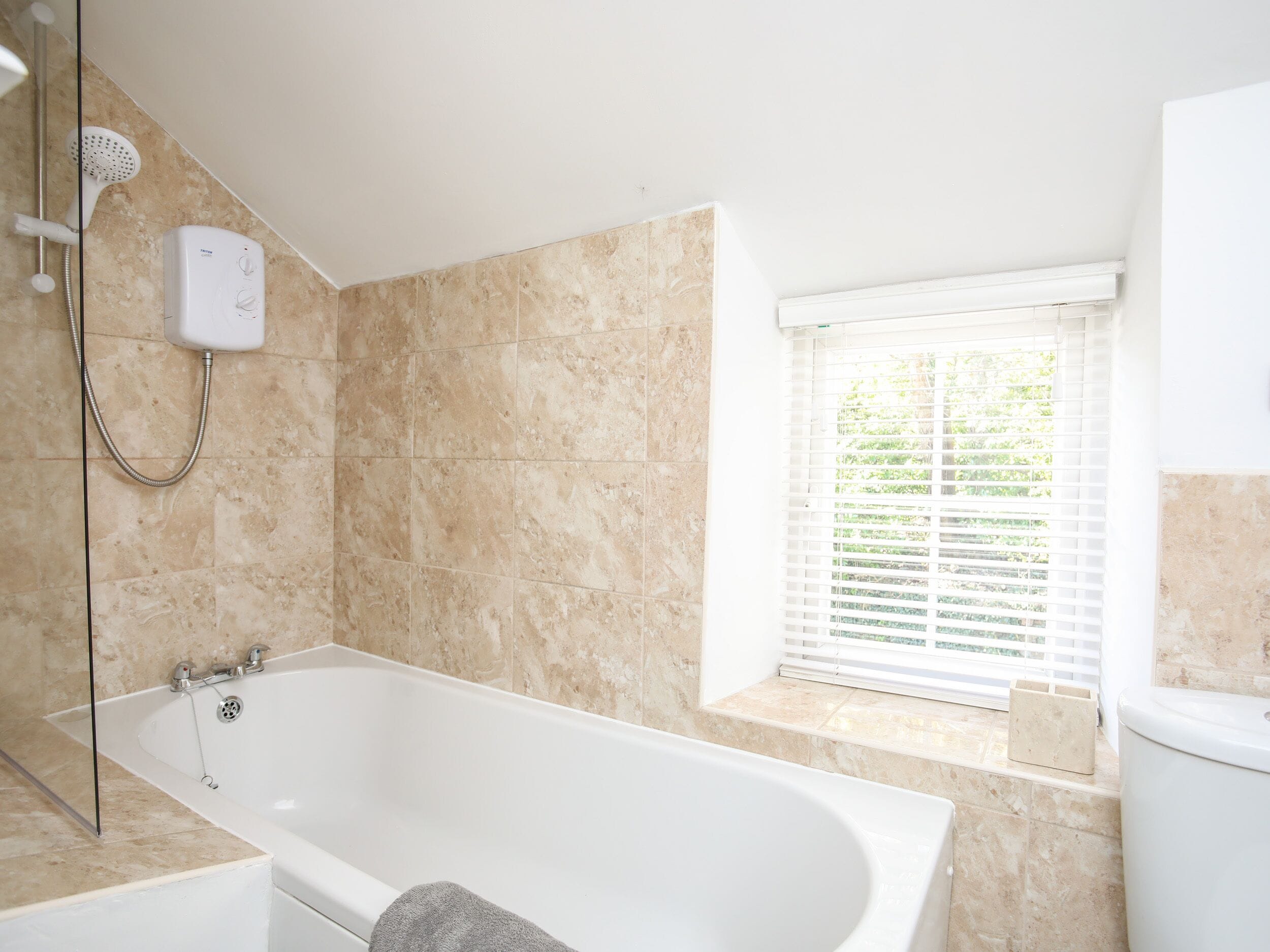 A modern bathroom with a freestanding bathtub, a handheld showerhead, and a window with blinds.