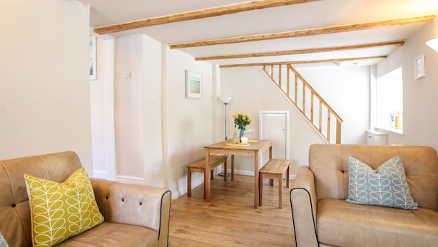 A spacious living room with a wooden staircase, leather sofas, and a wooden dining table. - Bryn Coed (Porthmadog)