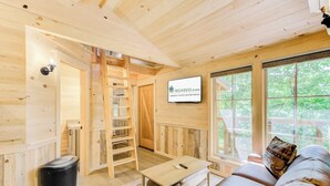 Interior de uma cabana de madeira com quarto no mezanino, área de jantar e sala de estar com vista para o exterior.