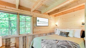 A cozy wooden cabin bedroom with a bed, pillows, and a sign indicating it's managed by Ayres Vacation Rentals.