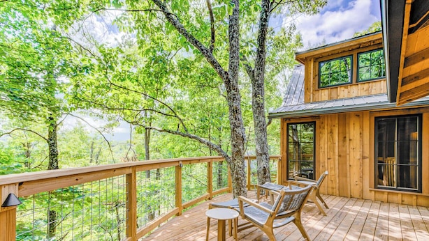 A wooden deck with a table and chairs, surrounded by trees and a view of the forest.
