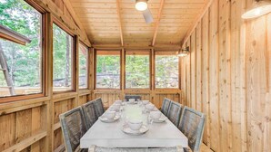 A wooden cabin with a dining table set for six, large windows, and a ceiling fan.