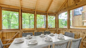 Eine Holzhütte mit einem für sechs Personen gedeckten Esstisch, großen Fenstern und Blick auf Bäume.