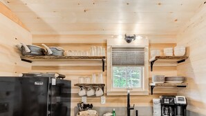 Een kleine keuken met een zwarte koelkast, een koffiezetapparaat en planken met servies en glazen.