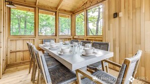 Una baita di legno con un tavolo da pranzo imbandito per sei persone, circondata da sedie in vimini, ampie finestre e un soffitto in legno.
