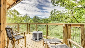 Eine Holzterrasse mit zwei Korbstühlen und einem runden Tisch, mit Blick auf eine üppige grüne Landschaft.