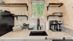 A modern kitchen with wooden walls, a black refrigerator, and a coffee machine. - Outdoor Shower Treehouse in Smokies | Cottonwood (Sevierville)