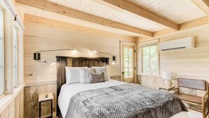 Une chambre confortable avec un plafond en bois, un lit recouvert d’une couverture à motifs, une table de chevet et un bureau avec une lampe.