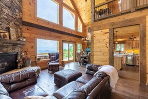 A spacious living area with a fireplace, leather sofas, and a dining table. - Blue Ridge Skylodge-Mountain Views - Hot Tub - Fire Pit -4WD-AWD (Bryson City)