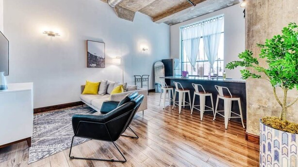 A modern living room with a sofa, black chair, and a dining area with bar stools. - Sosuite | 2BR Apt w W/D, Gym, On-Site Restaurant (Philadelphia)