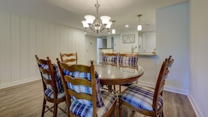 A dining area with a round table, four wooden chairs with plaid cushions, a chandelier, and a kitchen in the background. - 525 Plantation Club: Stylish Villa, 2 Bedrooms, Sleeps 6, Free Bikes, Pool (Hilton Head Island)