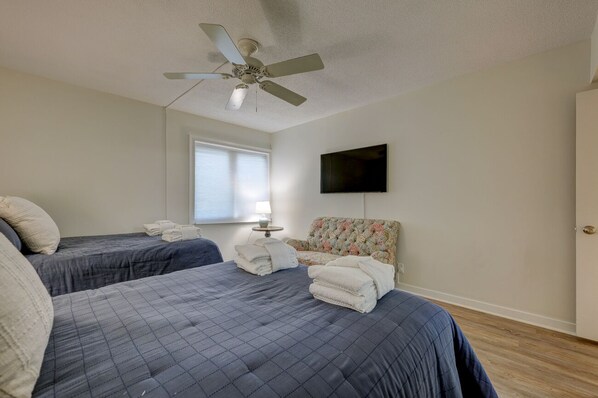 A hotel room with two beds, a ceiling fan, a TV, and a window with blinds.