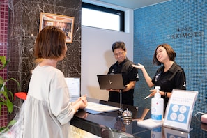 Guests are greeted by a sleek reception area with a glass reception desk, framed artwork, and convenient amenities.