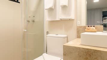 A modern bathroom with a glass shower enclosure, a white toilet, and a marble countertop with a sink and mirror.