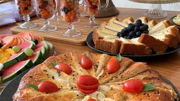 A table with a variety of food items including a fruit bowl, a cake, and a bread dish.