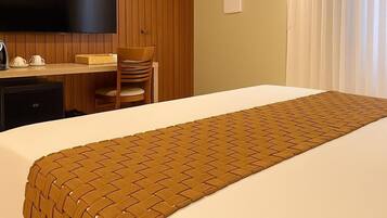 Una habitación de hotel con cama, escritorio, silla, televisor y ventana con cortinas.