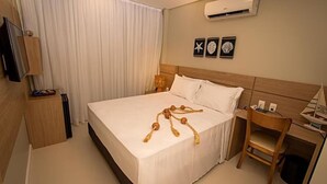 Habitación de hotel con cama, escritorio, silla, televisor y aire acondicionado instalado en la pared.