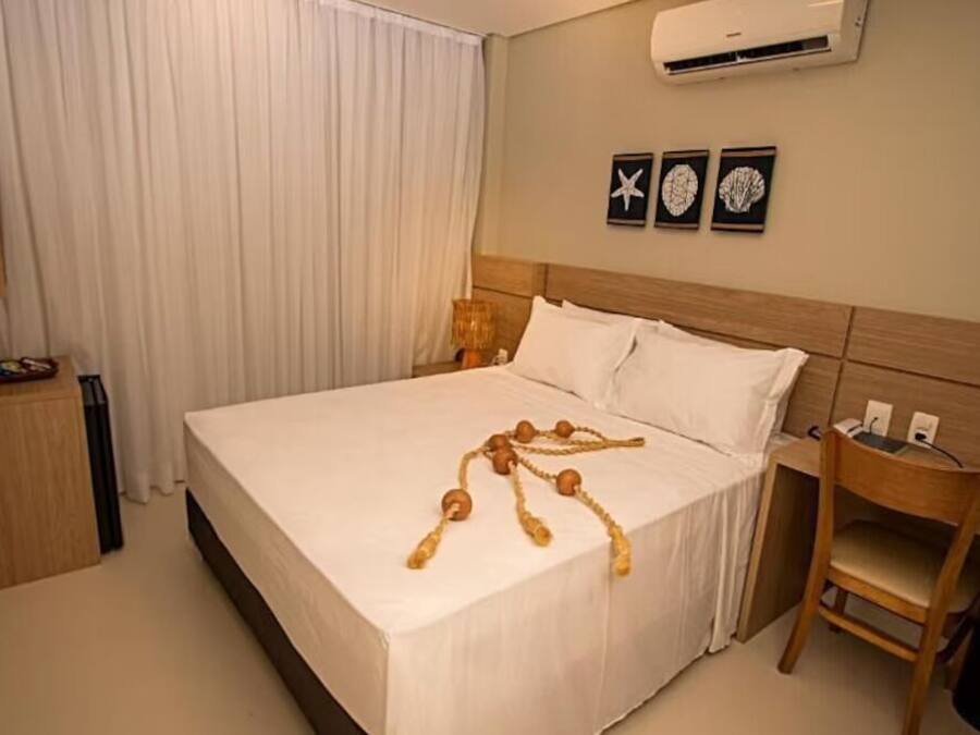 A hotel room with a bed, a desk, a chair, a TV, and a wall-mounted air conditioner.