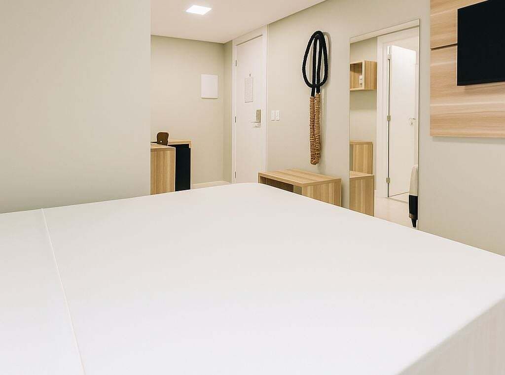Een hotelkamer met een groot bed, een bureau, een stoel, een spiegel en een aan de muur bevestigde televisie.