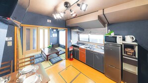 A compact kitchen with a microwave, stove, and refrigerator. There is a dining area with a table set for two and a small window. - HOTEL Kita-Shinagawa (Tokyo)