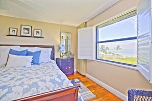 A bedroom with a large bed, a dresser, a mirror, and a window with a view of the beach. - Tarpon Beach 112 offers the BEST Beach View! Stunning, Top Floor, Corner Unit (Sanibel)