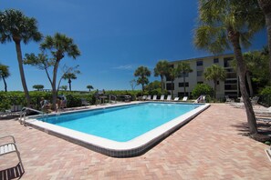 A rectangular swimming pool with a tiled edge, surrounded by lounge chairs and palm trees, set against a backdrop of a multi-story building. - Tarpon Beach 112 offers the BEST Beach View! Stunning, Top Floor, Corner Unit (Sanibel)