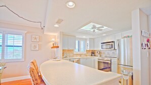 A kitchen with white cabinets, a central island, a microwave, a refrigerator, and a ceiling fan. - Tarpon Beach 112 offers the BEST Beach View! Stunning, Top Floor, Corner Unit (Sanibel)