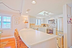 A kitchen with white cabinets, a central island, a microwave, a refrigerator, and a ceiling fan. - Tarpon Beach 112 offers the BEST Beach View! Stunning, Top Floor, Corner Unit (Sanibel)