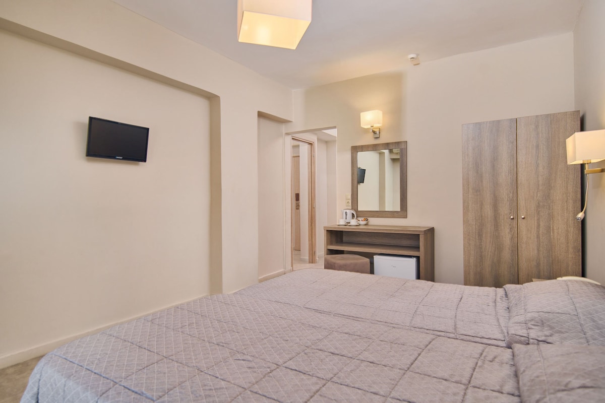 Ein Hotelzimmer mit Bett, Wandfernseher, Schminktisch mit Spiegel und Kleiderschrank.