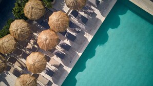 Vista aérea de una zona de piscina con sombrillas de techo de paja y sillones de relax.