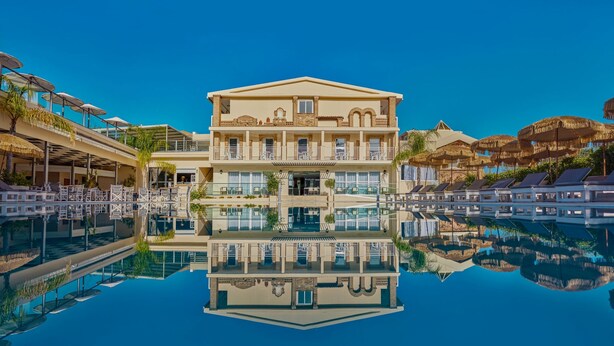 Un hotel con una piscina grande, varios balcones y un reflejo en el agua.