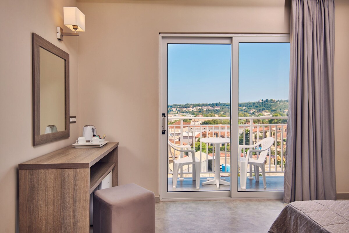Ein Hotelzimmer mit Balkon, einem Schreibtisch mit Kaffeemaschine und einem Bett.