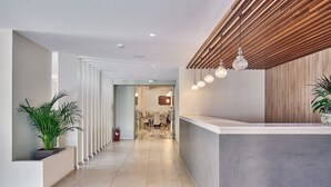 Una zona de recepción moderna con techo de madera, un mostrador de recepción y un pasillo que conduce a un comedor.