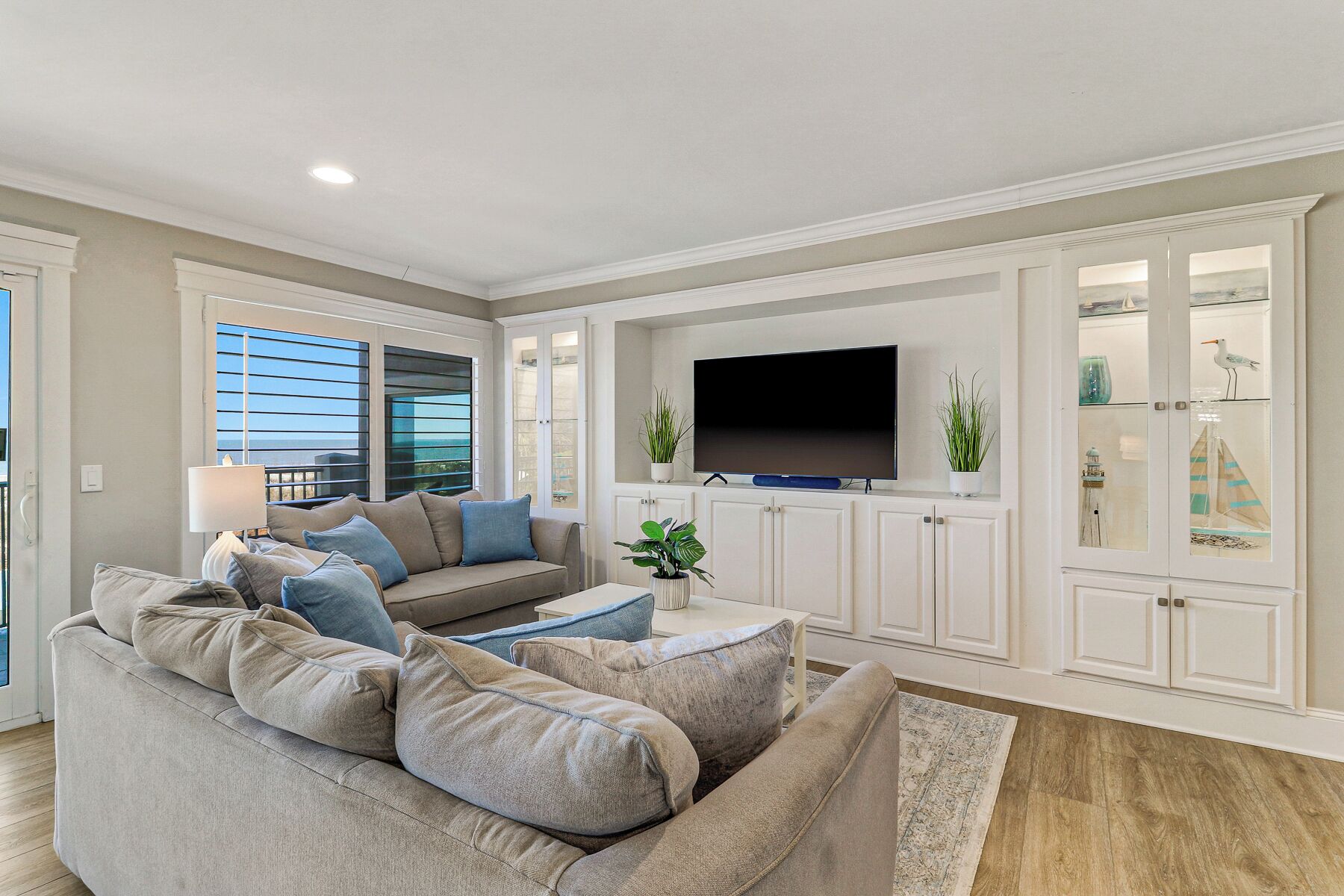 A living room with a beige sofa, a flat-screen TV, and a cabinet with glass doors.