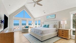 Ein Schlafzimmer mit einem großen Bett, einem Fernseher, einem Deckenventilator und Meerblick durch große Fenster.