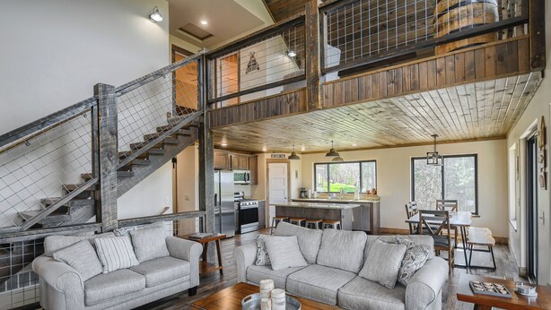 A spacious living area with a large gray sectional sofa, a wooden coffee table, and a kitchen in the background. - Views for Days, New Cabin Near Terry Peak Ski Area w/ Hot Tub and Large Deck! (Lead)