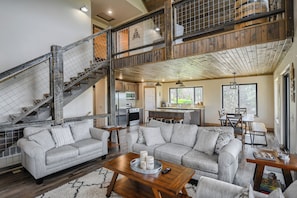 Relax in this inviting living space with a large sofa, wooden beams, and a staircase leading to an upper level.